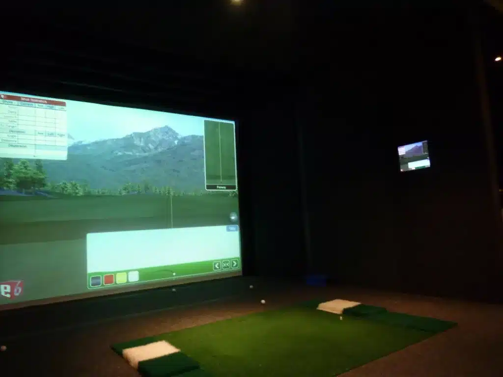 a man playing golf on a screen with a video game - File:Indoor golf simulator.JPG